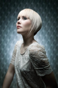 Ein junges weibliches Model mit einem modernen blonden Kurzhaarschnitt und ausdrucksstarkem Make-Up blickt nachdenklich nach schräg oben.