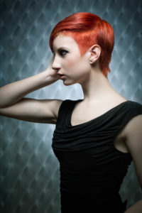 Eine junge Frau mit einem modernen Kurzhaarschnitt in einer leuchtend roten Farbe. Sie trägt einen Undercut.