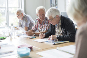 In einem Büro sitzen mehrere ältere Personen an einem Gruppentisch und schauen gemeinsam Lernunterlagen an. In einem Büro sitzen mehrere ältere Personen an einem Gruppentisch und schauen gemeinsam Lernunterlagen an.