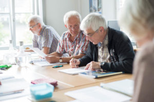 In einem Büro sitzen mehrere ältere Personen an einem Gruppentisch und schauen gemeinsam Lernunterlagen an.