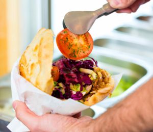 Ein Mitarbeiter füllt ein aufgeklapptes Brötchen mit Tomaten, Gurken, Rotkraut, Salat und Dönerfleisch. Ein Mitarbeiter füllt ein aufgeklapptes Brötchen mit Tomaten, Gurken, Rotkraut, Salat und Dönerfleisch.