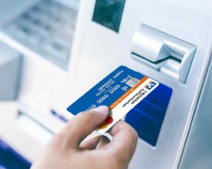 Eine Person führt eine Geldkarte der Volksbanken Raiffeisenbanken zum Kartenschlitz eines Geldautomaten.