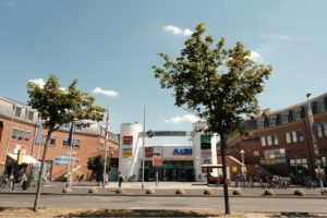 Über dem Haupteingang des Seidnitz Centers sehen wir blauen Himmel mit wenigen Wolken. Im Vordergrund befindet sich die Straße mit zwei Bäumen. Über dem Haupteingang des Seidnitz Centers sehen wir blauen Himmel mit wenigen Wolken. Im Vordergrund befindet sich die Straße mit zwei Bäumen.