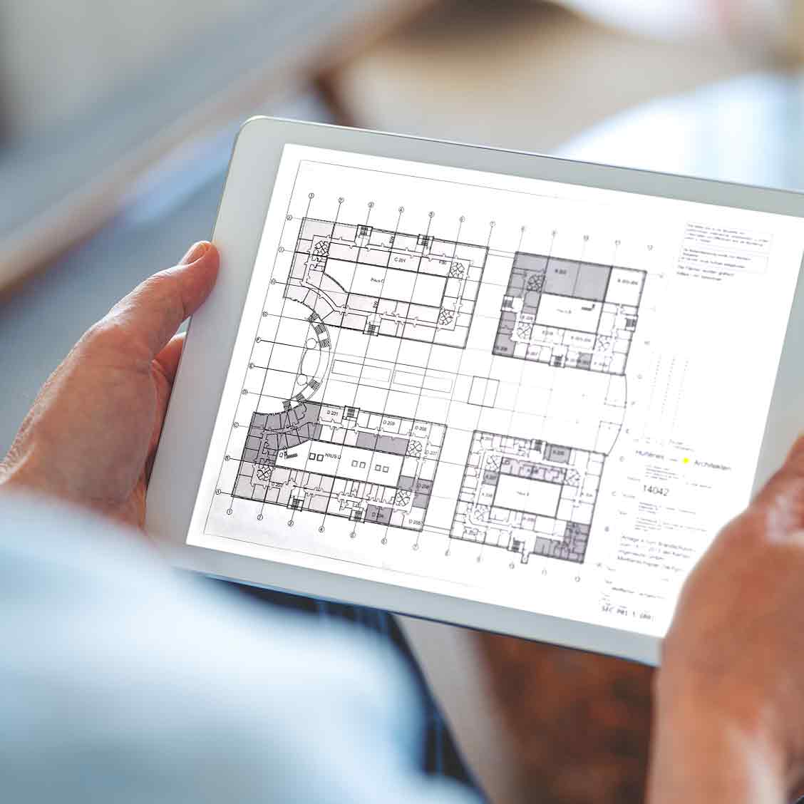 Wir blicken über die Schulter einer Person, welche ein Tablet in Händen hält und darauf einen Lageplan betrachtet.